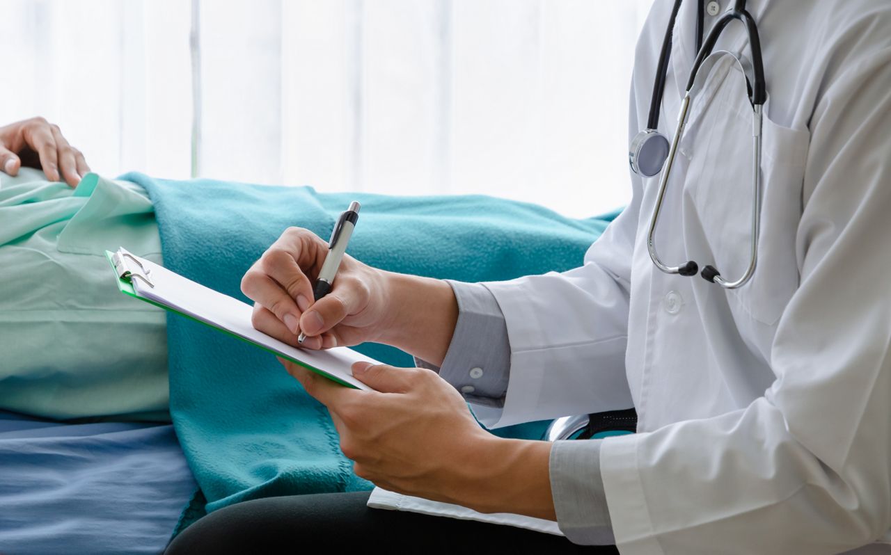 Close up of doctor writing on a medical chart with patient lying on hospital bed. Healthcare and insurance concept; Shutterstock ID 1797121909; purchase_order: DNC Thumbnails; job: Webinars 3 (50/188); client: ; other: 