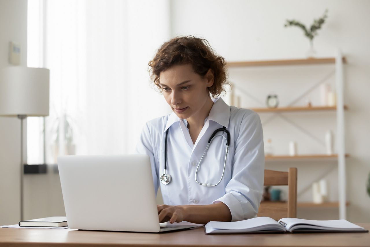 Serious woman wearing white uniform with stethoscope working on laptop, sitting at desk in hospital, focused doctor physician gp looking at computer screen, using medical apps, consulting online; Shutterstock ID 1807046479; purchase_order: DNC Thumbnails; job: Courses; client: ; other: Replace Fishwife