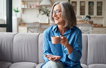 Happy beautiful relaxed mature older adult grey-haired woman drinking coffee relaxing on sofa at home. Smiling stylish middle aged 60s lady enjoying resting sitting on couch in modern living room.; Shutterstock ID 1818491870; purchase_order: DNC Thumbnails; job: Webinars 4 ; client: ; other: 