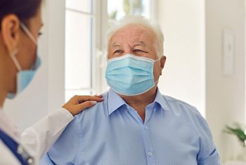 Trust and support. Happy senior patient and doctor, wearing medical face masks, communicating in hospital office. General practitioner in modern clinic patting aged man on the shoulder cheering him up; Shutterstock ID 1822742396; purchase_order: DNC Thumbnails; job: Publications; client: ; other: 