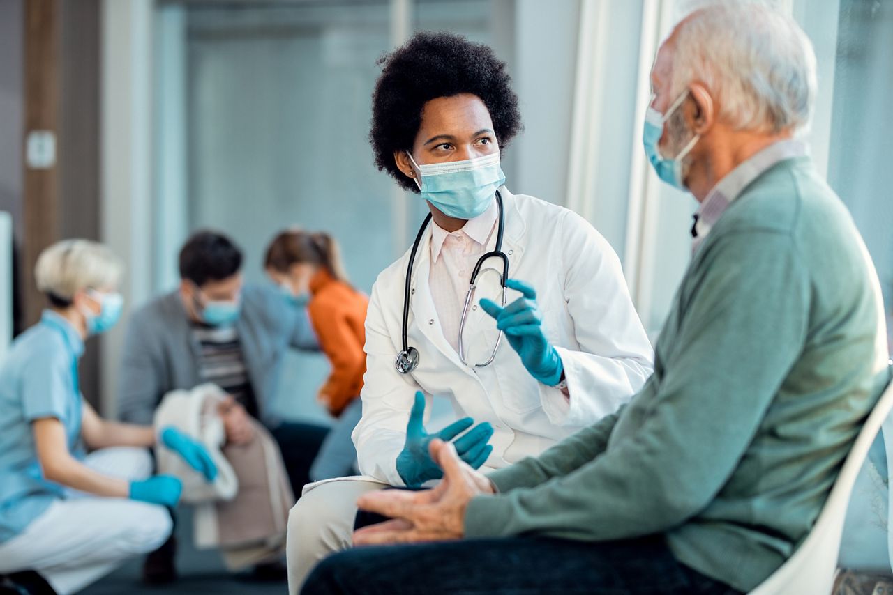 Black female doctor and senior man wearing protective face masks while communicating in a waiting room at hospital. ; Shutterstock ID 1865726542; purchase_order: DNC Thumbnails; job: Webinars 3 (50/188); client: ; other: 