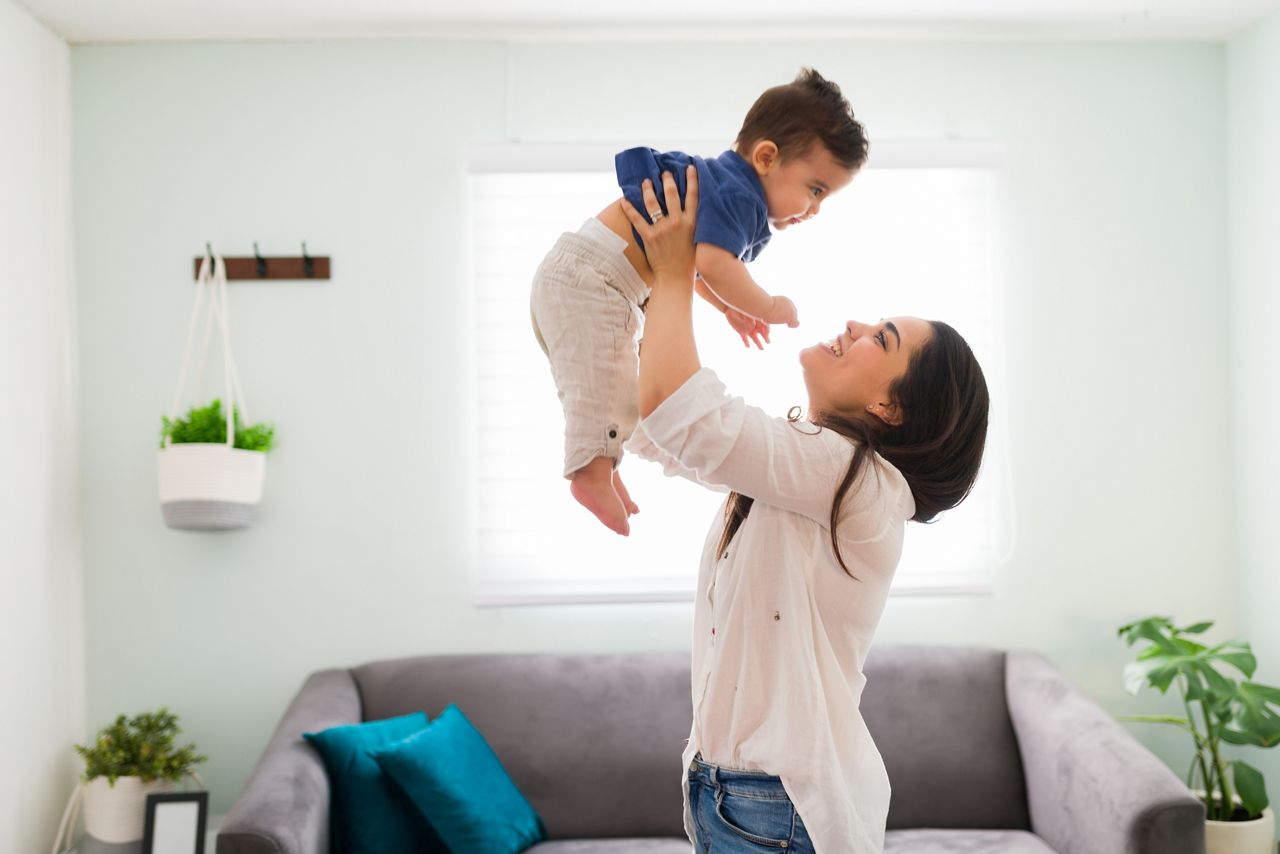 Happy young woman holding up her baby boy up while standing in living room; Shutterstock ID 1870861414; purchase_order: DNC Thumbnails; job: Webinars 4 ; client: ; other: 