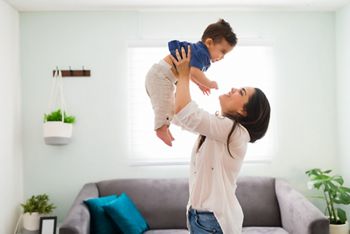 Happy young woman holding up her baby boy up while standing in living room; Shutterstock ID 1870861414; purchase_order: DNC Thumbnails; job: Webinars 4 ; client: ; other: 