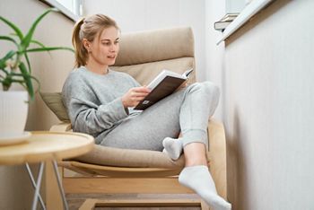 Blonde woman reading book while sitting on beige armchair in apartment; Shutterstock ID 1890216391; purchase_order: DNC Thumbnails; job: Webinars 1 (50/189); client: ; other: 