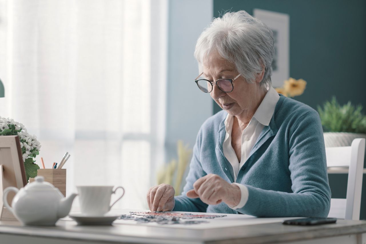 Happy senior woman playing puzzle at home alone and having tea; Shutterstock ID 1921919486; purchase_order: DNC Thumbnails; job: Videos; client: ; other: 