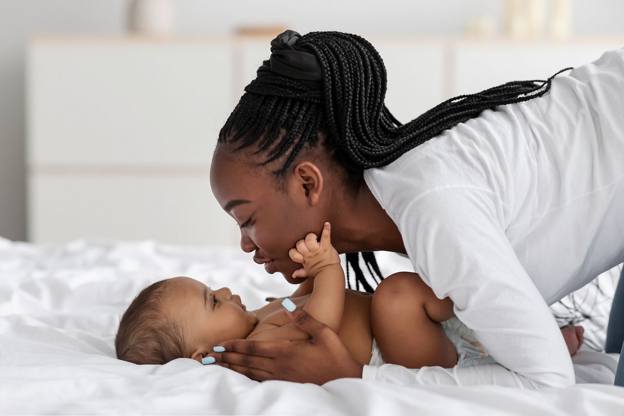Black mom playing in bed with her infant, kissing baby; Shutterstock ID 1940935138; purchase_order: DNC Thumbnails; job: Webinars 4 ; client: ; other: 