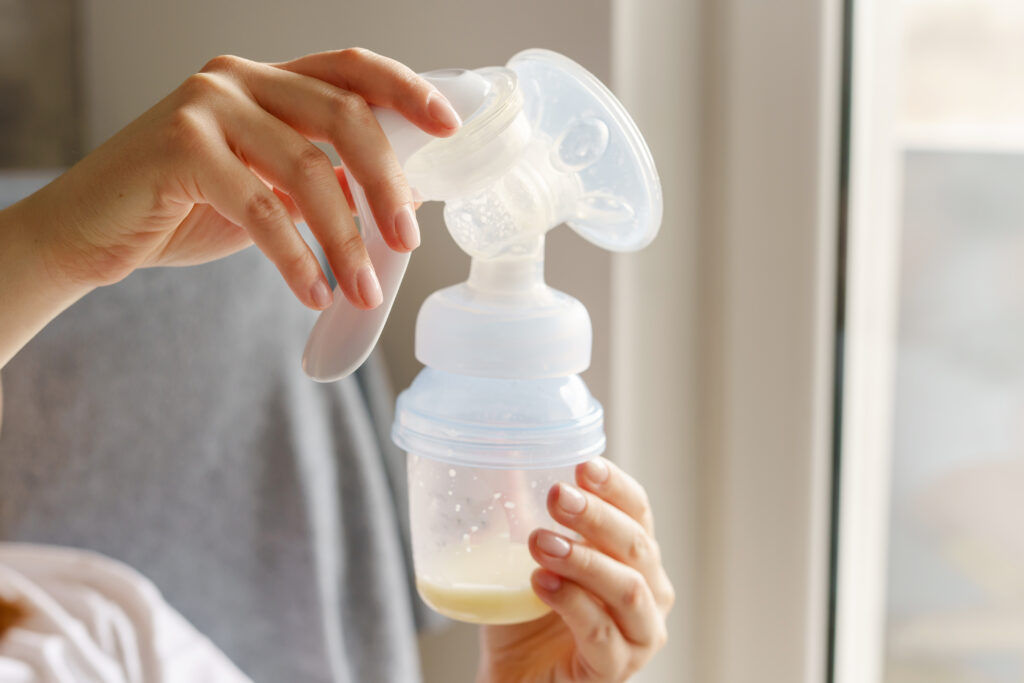 Close up on hands of unknown caucasian woman young mother using manual breast pump to get milk for supplementary feeding - Mother increase breast milk supply stimulating lactation for infant nutrition