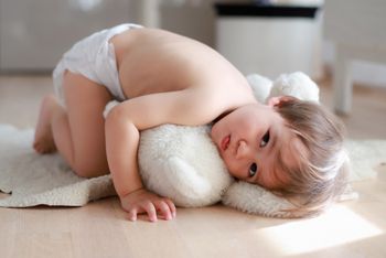 Adorable baby boy wearing diaper playing on the floor with teddy bear at home. Happy mixed race Asian-German infant lying and relaxing.; Shutterstock ID 1955538139; purchase_order: DNC Thumbnails; job: Infographics; client: ; other: 