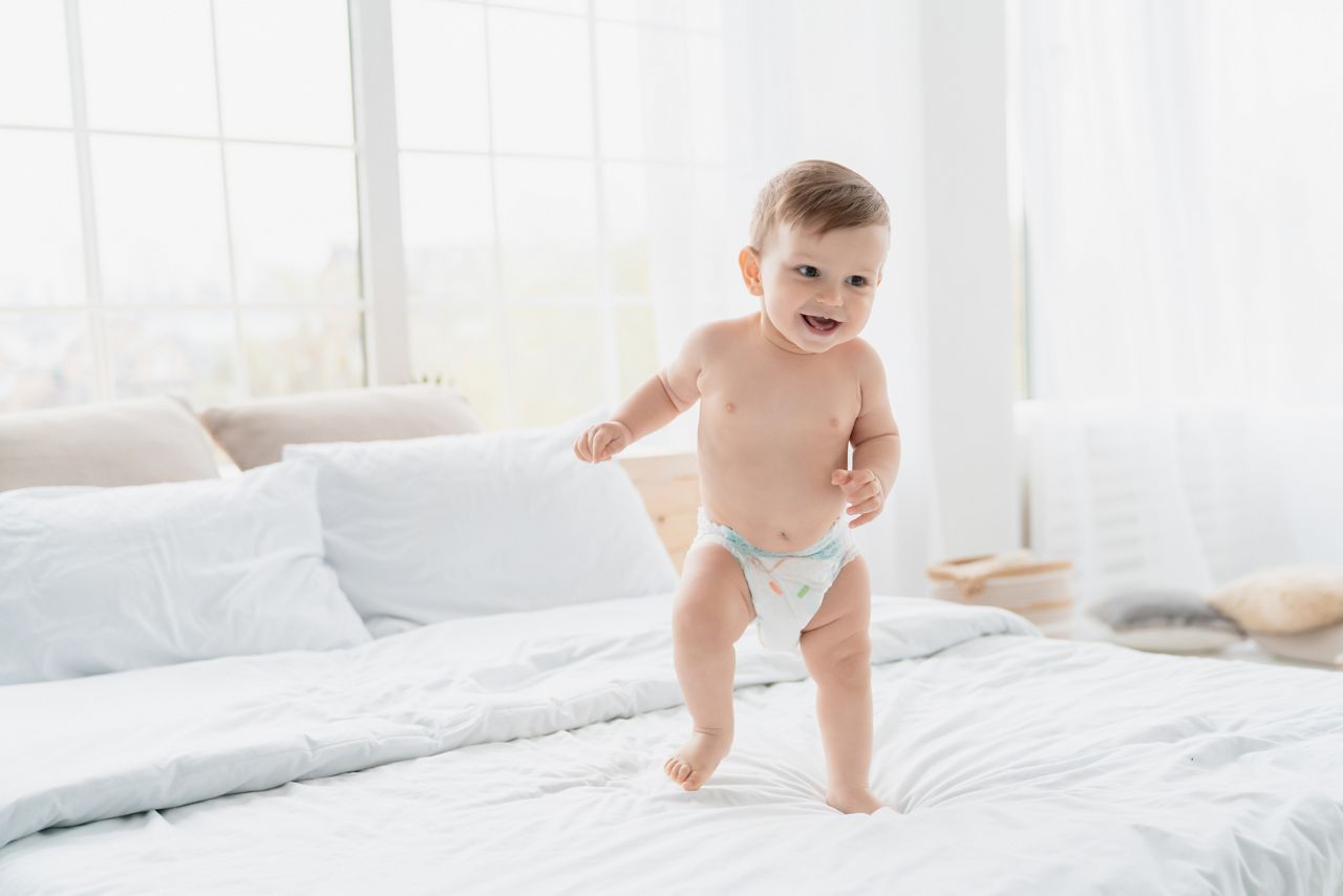 Small little caucasian baby newborn infant making first steps, cute toddler kid child girl son boy daughter learning walking creeping on the bed. Childcare and childhood concept; Shutterstock ID 2007312044; purchase_order: DNC Thumbnails; job: Infographics; client: ; other: 