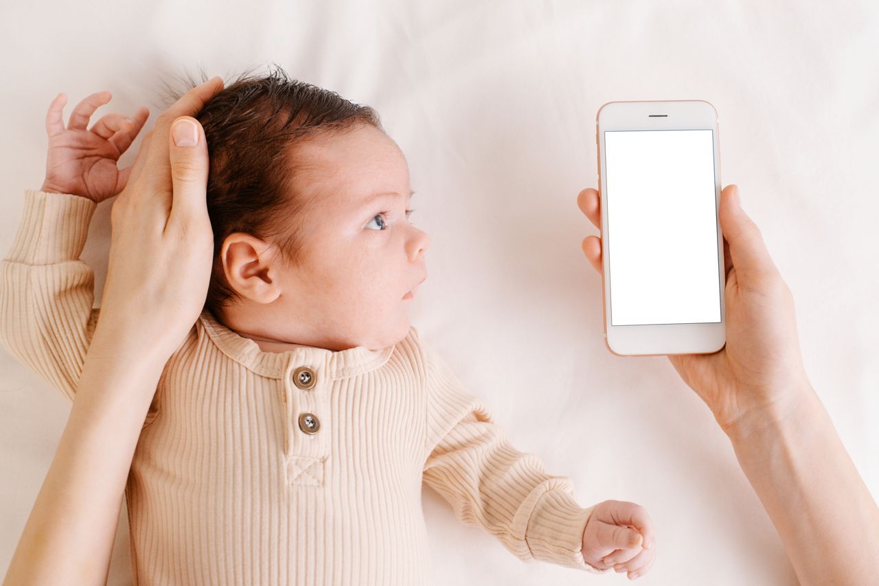 Baby newborn on white bed, woman holding mobile phone with white screen in hand top view.Technology and childhood concept; Shutterstock ID 2010221603; purchase_order: DNC Thumbnails; job: Webinars 3 (50/188); client: ; other: 