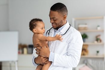 Portrait Of Handsome Young Black Pediatrician Holding Adorable Little Infant Boy In Hands, Cute Toddler Child Playing With Stethoscope On Doctor's Neck While Having Medical Check Up In Clinic; Shutterstock ID 2018780882; purchase_order: DNC Thumbnails; job: Webinars 1 (50/189); client: ; other: 