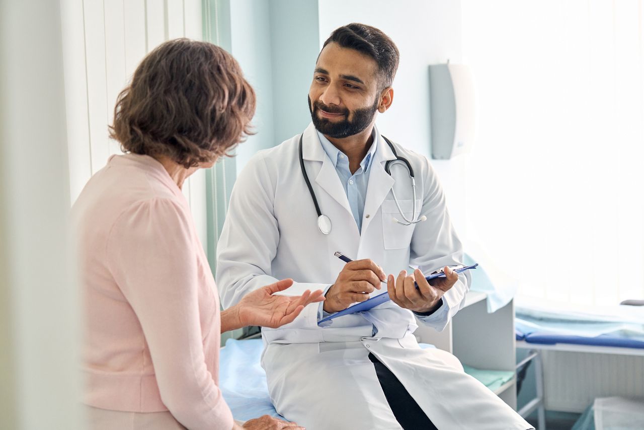 Indian male doctor consulting senior old patient filling form at consultation. Professional physician wearing white coat talking to mature woman signing medical paper at appointment visit in clinic.; Shutterstock ID 2036186195; purchase_order: DNC Thumbnails; job: Webinars 4 ; client: ; other: 