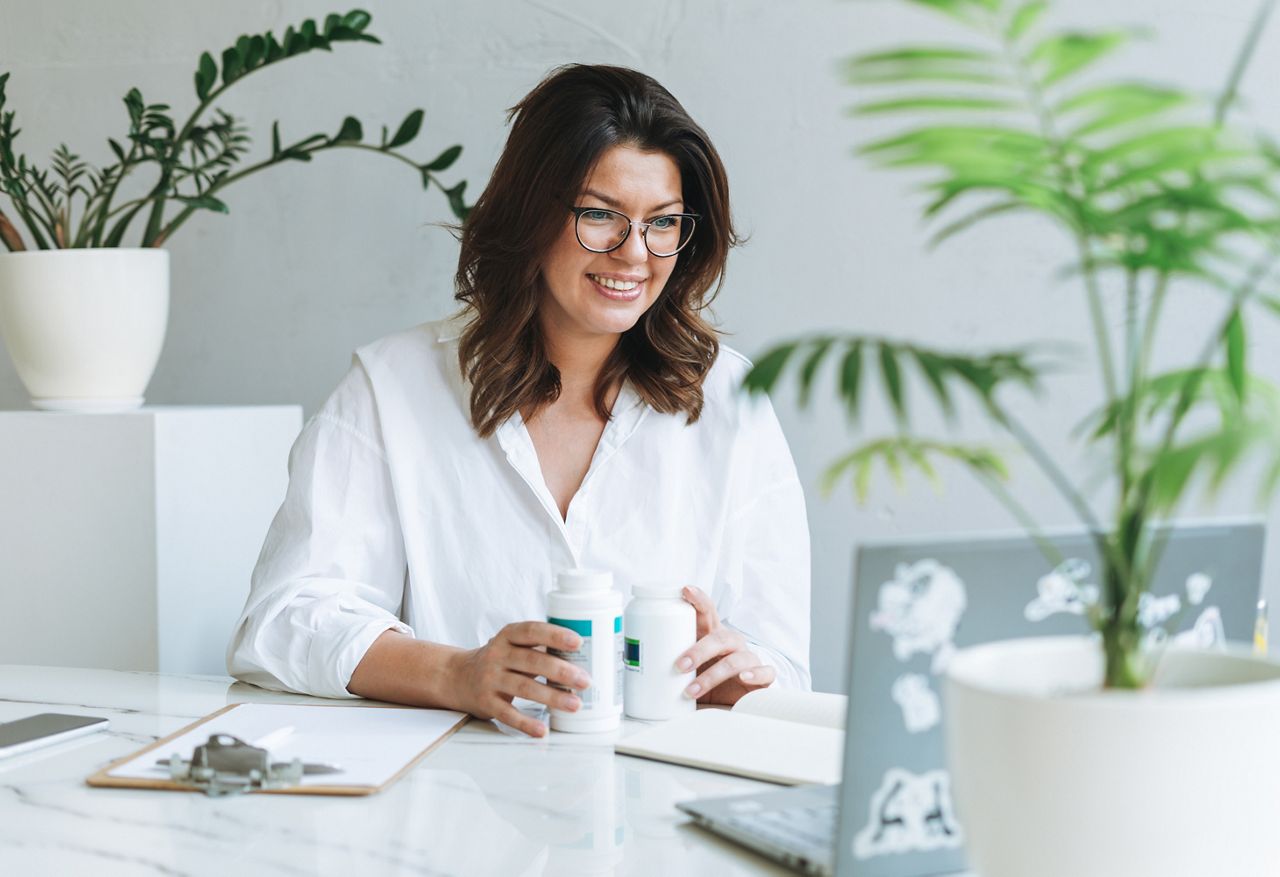 Young smiling brunette woman nutritionist plus size in white shirt working at laptop on table with house plant in bright modern office. Doctor communicates with patient online; Shutterstock ID 2038353506; purchase_order: DNC Thumbnails; job: Webinars 1 (50/189); client: ; other: 