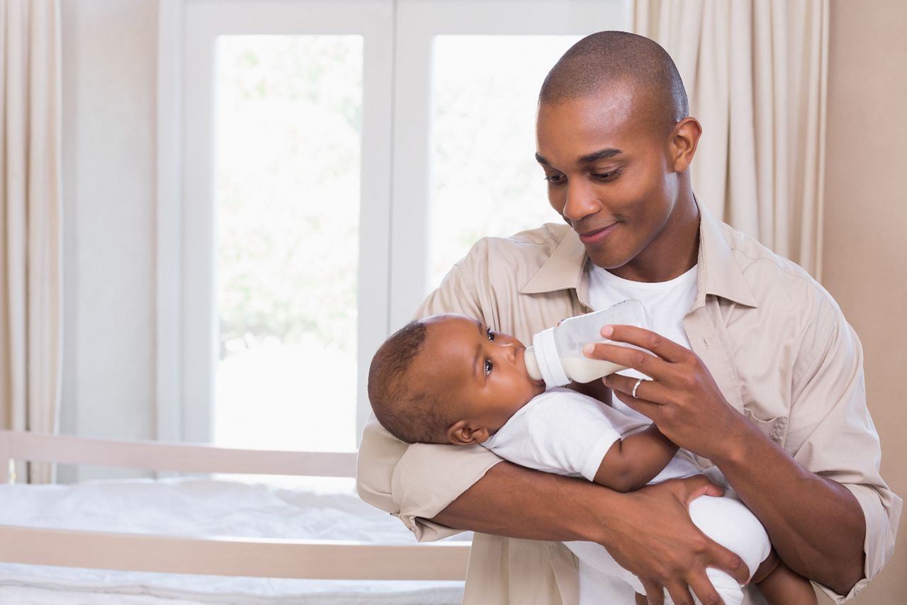 Happy father feeding his baby boy a bottle at home in the bedroom; Shutterstock ID 207783811; purchase_order: DNC Thumbnails; job: Webinars 3 (50/188); client: ; other: 