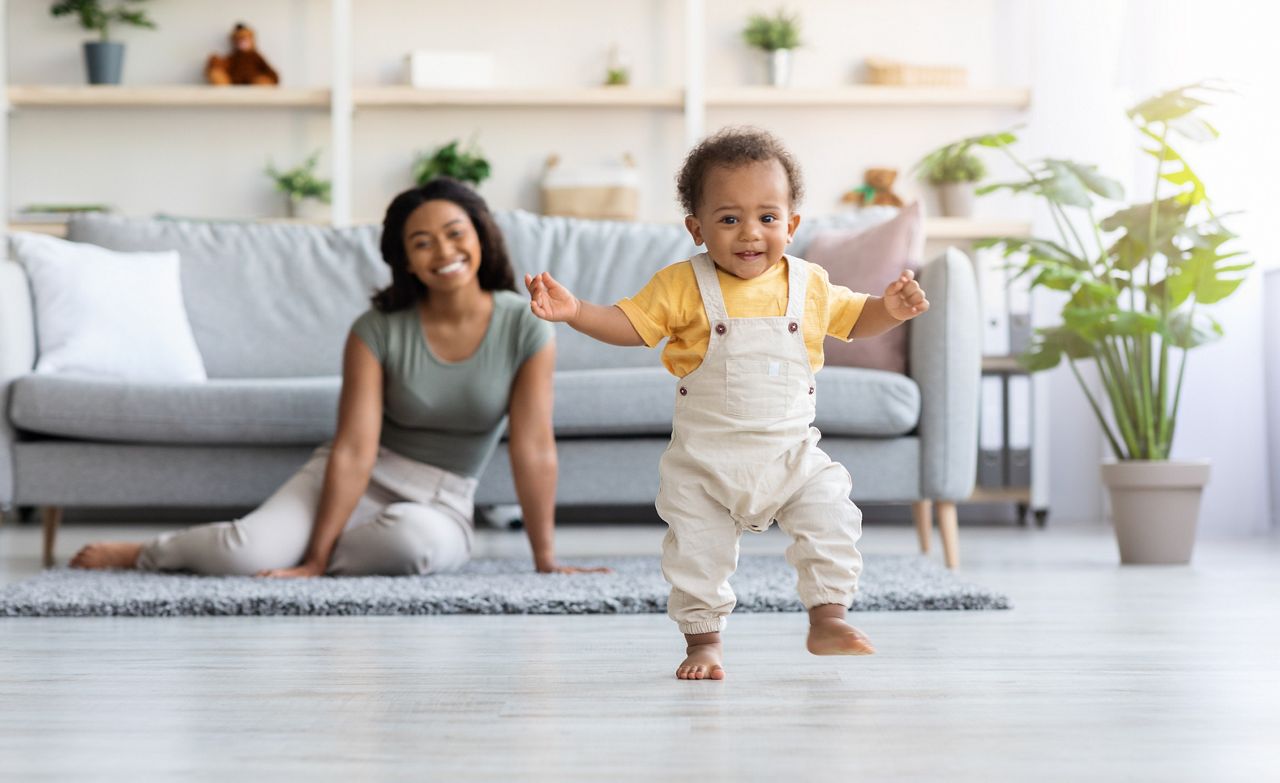 First Steps. Adorable Black Infant Child Walking In Living Room At Home, Cute African American Toddler Boy Stepping On Floor And Looking At Camera, His Proud Mother Smiling On Background, Free Space; Shutterstock ID 2100636871; purchase_order: 25 thumbnail photos ; job: ; client: ; other: 