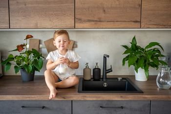 Happy baby girl sitting at the table in the kitchen and drinking milk. High quality photo; Shutterstock ID 2108422982; purchase_order: DNC Thumbnails; job: Webinars 2 (50/188); client: ; other: 