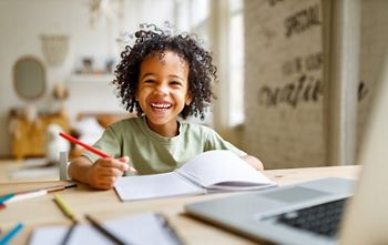 Distance education. Smiling african american child schoolboy  studying online on laptop at home, sitting at table and communicating with teacher through video call on computer; Shutterstock ID 2112109130; purchase_order: DNC Thumbnails; job: Articles; client: ; other: 