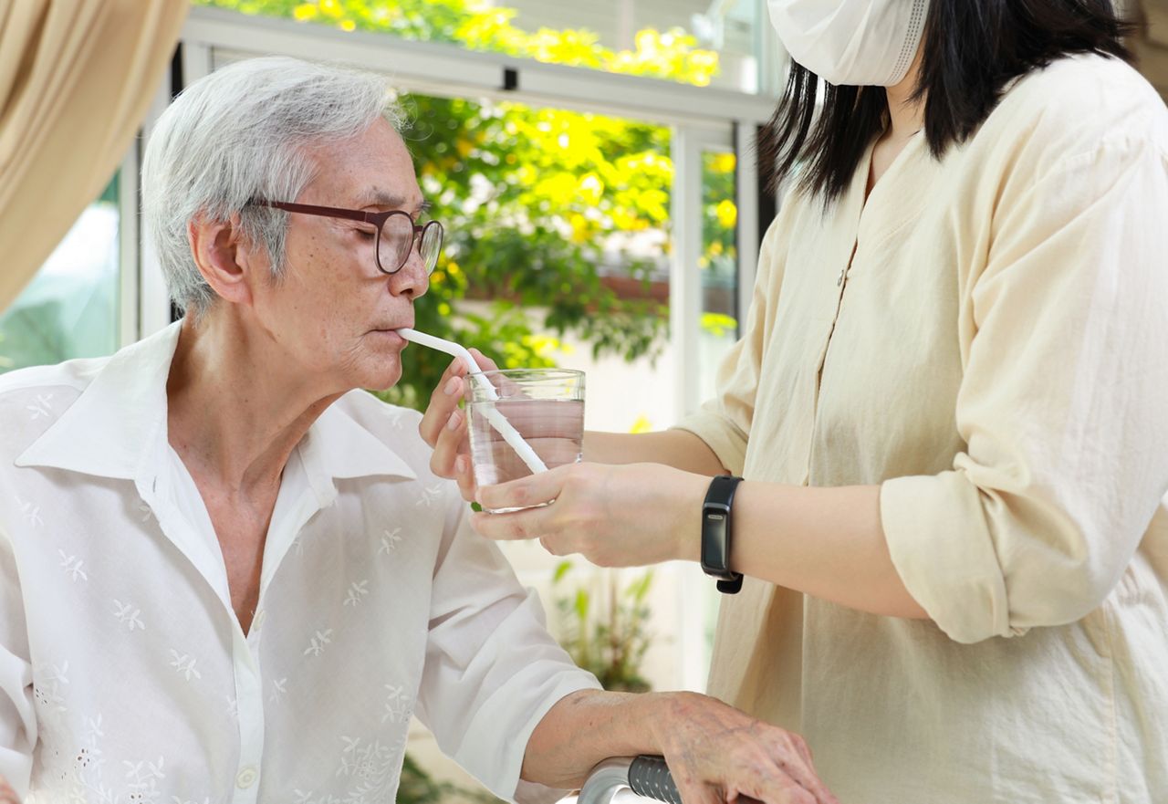 Asian caregiver take care of senior woman give drinking water from a glass,feeding water using a straw to prevent choking at nursing home,thirsty elderly patient sucking water through straw for safety