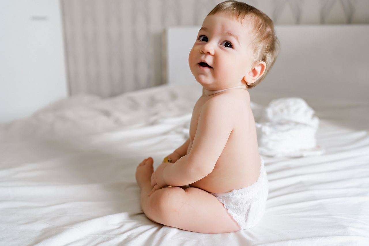 Infant baby kid sitting back happy smiling sitting on white bed at home; Shutterstock ID 2143148371; purchase_order: DNC Thumbnails; job: Videos; client: ; other: 