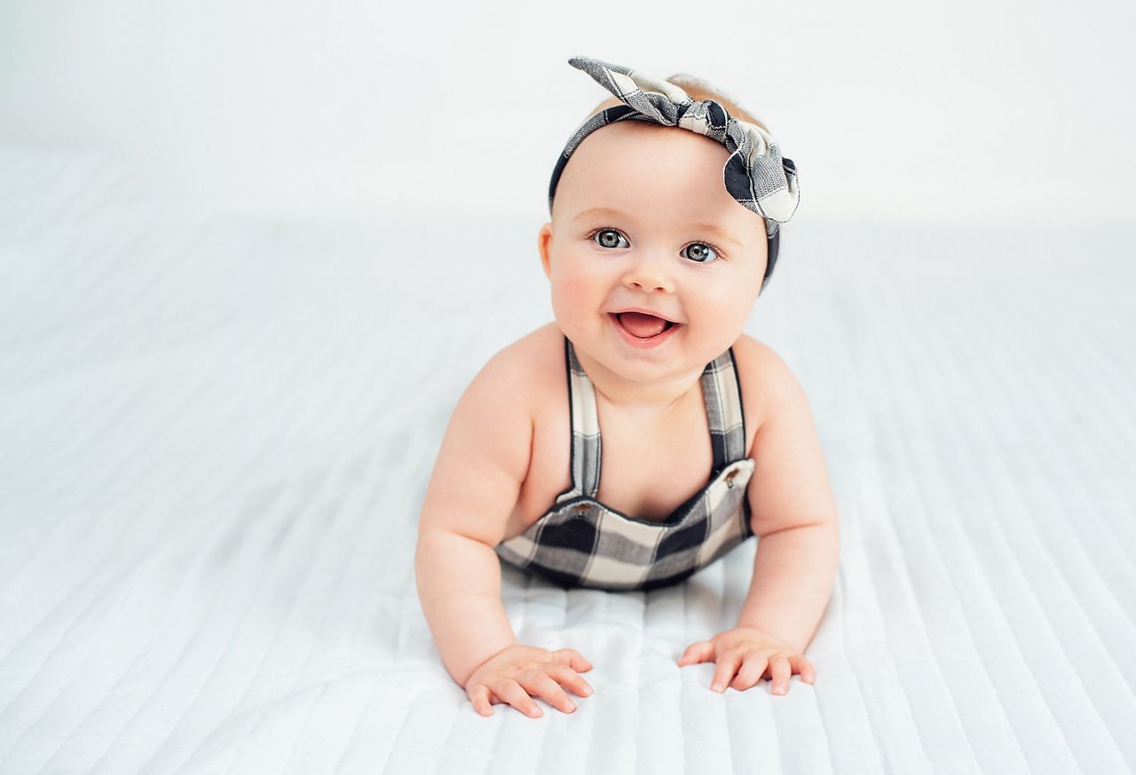 Seven month old baby child sitting on bed. Cute smiling little infant girl on white soft blanket. girl wearing headband. Charming blue eyed baby. Copy space.; Shutterstock ID 2147379339; purchase_order: DNC Thumbnails; job: Webinars 2 (50/188); client: ; other: 