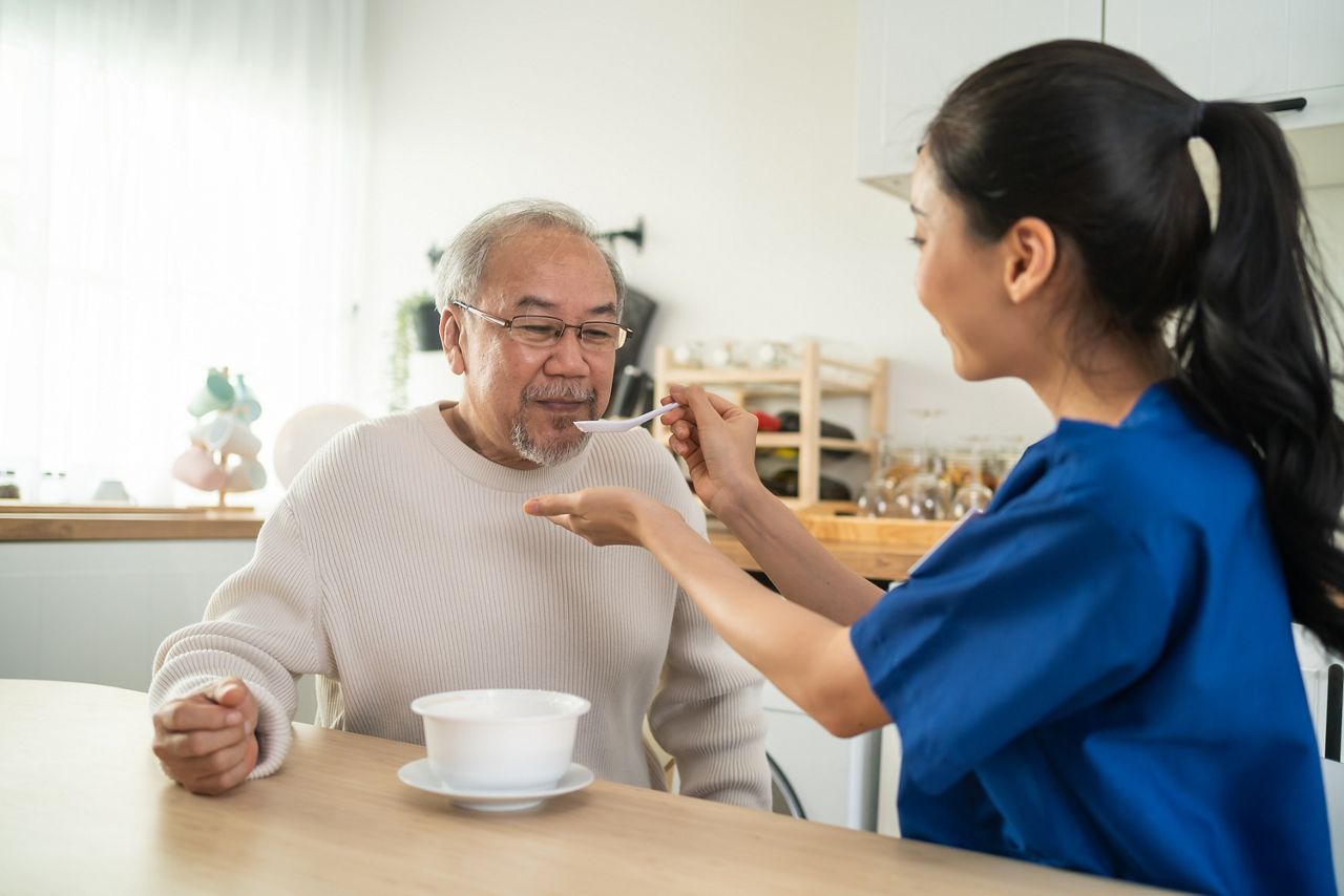 Asian caregiver nurse serve food to senior man sitting on dinner table. Attractive young specialist carer woman doctor support and taking care of happy older elderly mature grandfather at nursing home; Shutterstock ID 2153724325; purchase_order: DNC Thumbnails; job: Webinars 3 (50/188); client: ; other: 