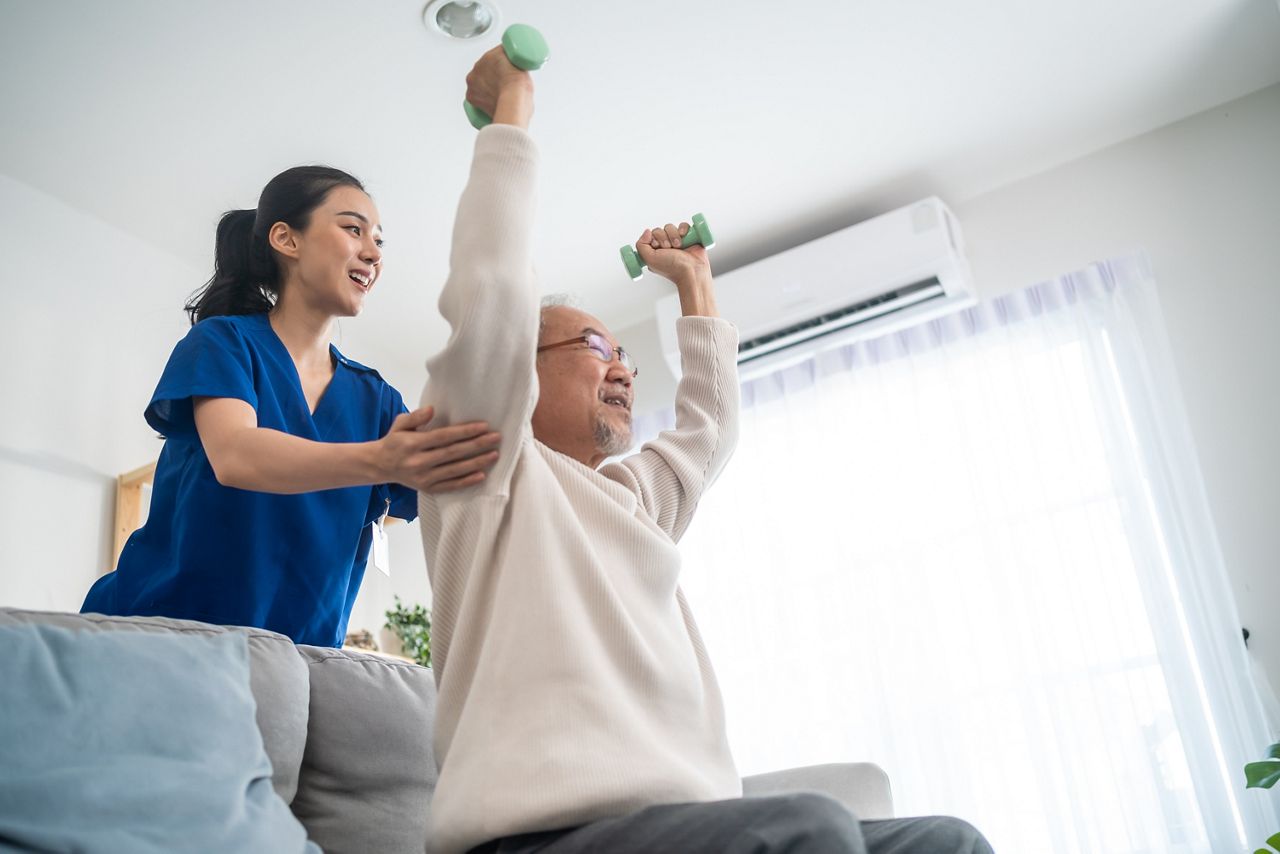 Asian older aged man doing physiotherapist with support from nurse. Senior elderly male sitting on sofa in living room using dumbbells workout exercise for patient with caregiver in nursing care.; Shutterstock ID 2157129949; purchase_order: 25 thumbnail photos ; job: ; client: ; other: 
