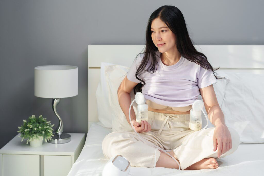 happy mother using breast pump machine to pumping milk for her newborn baby on a bed