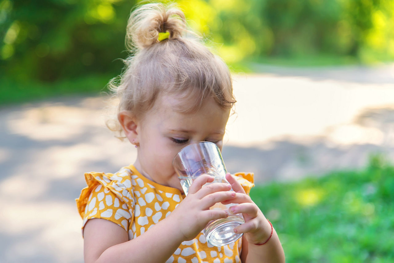 The child drinks water from a glass. Selective focus. Kid.