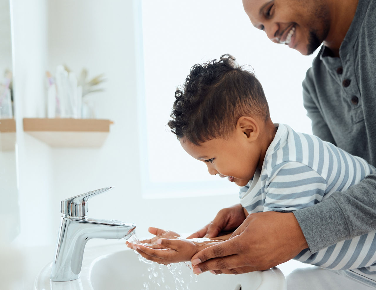 Wash them thoroughly. Shot of an adorable little boy washing his hands with the help of his father at home.