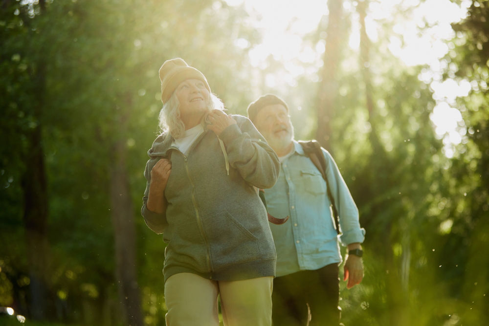 Senior couple, man and woman taking peaceful walk in park, enjoying tranquility and the beauty of nature. Sunlight and greenery. Concept of sport, aging, active and healthy lifestyle, health care