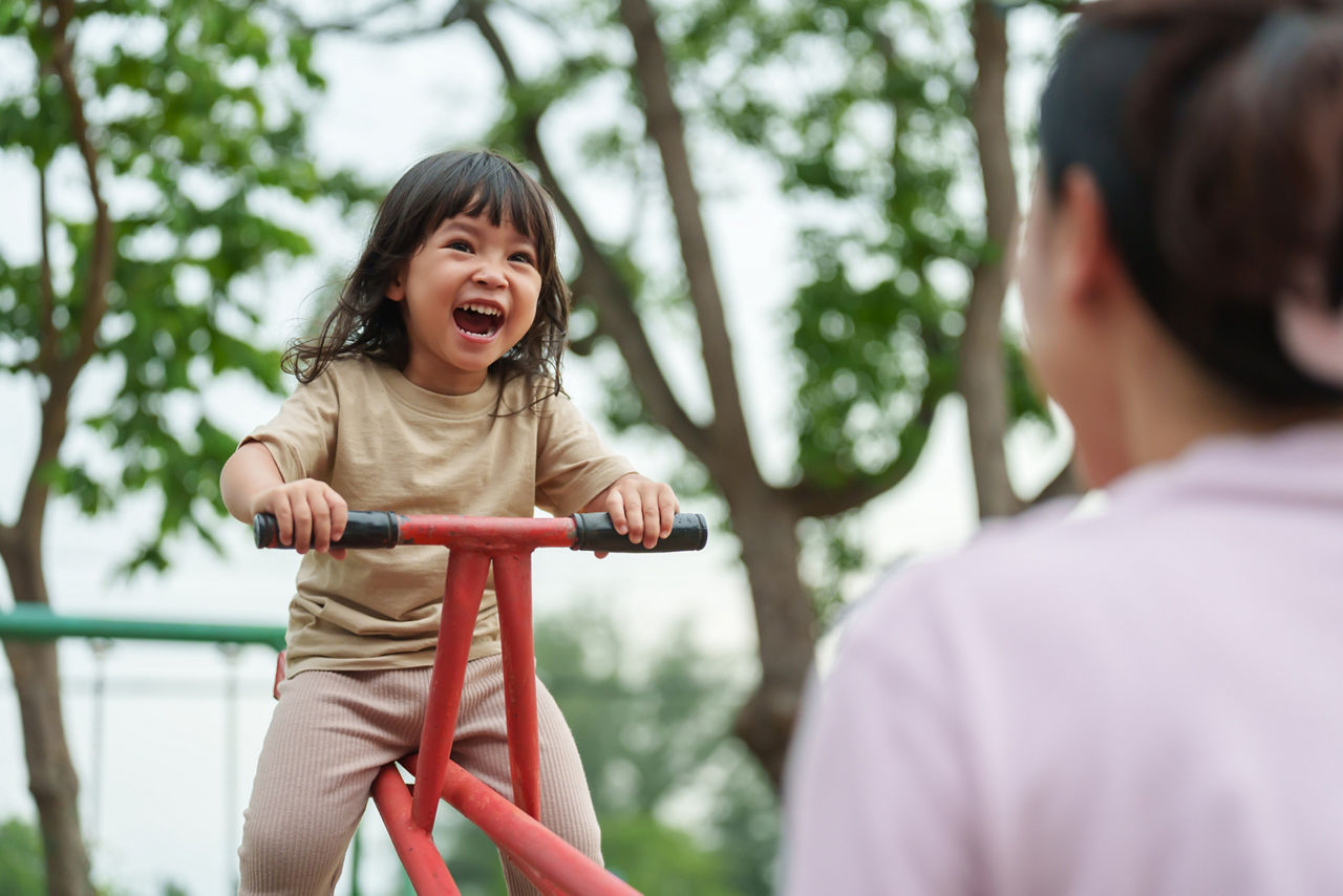 toddler girl and mother playing seesaw in outdoor playground