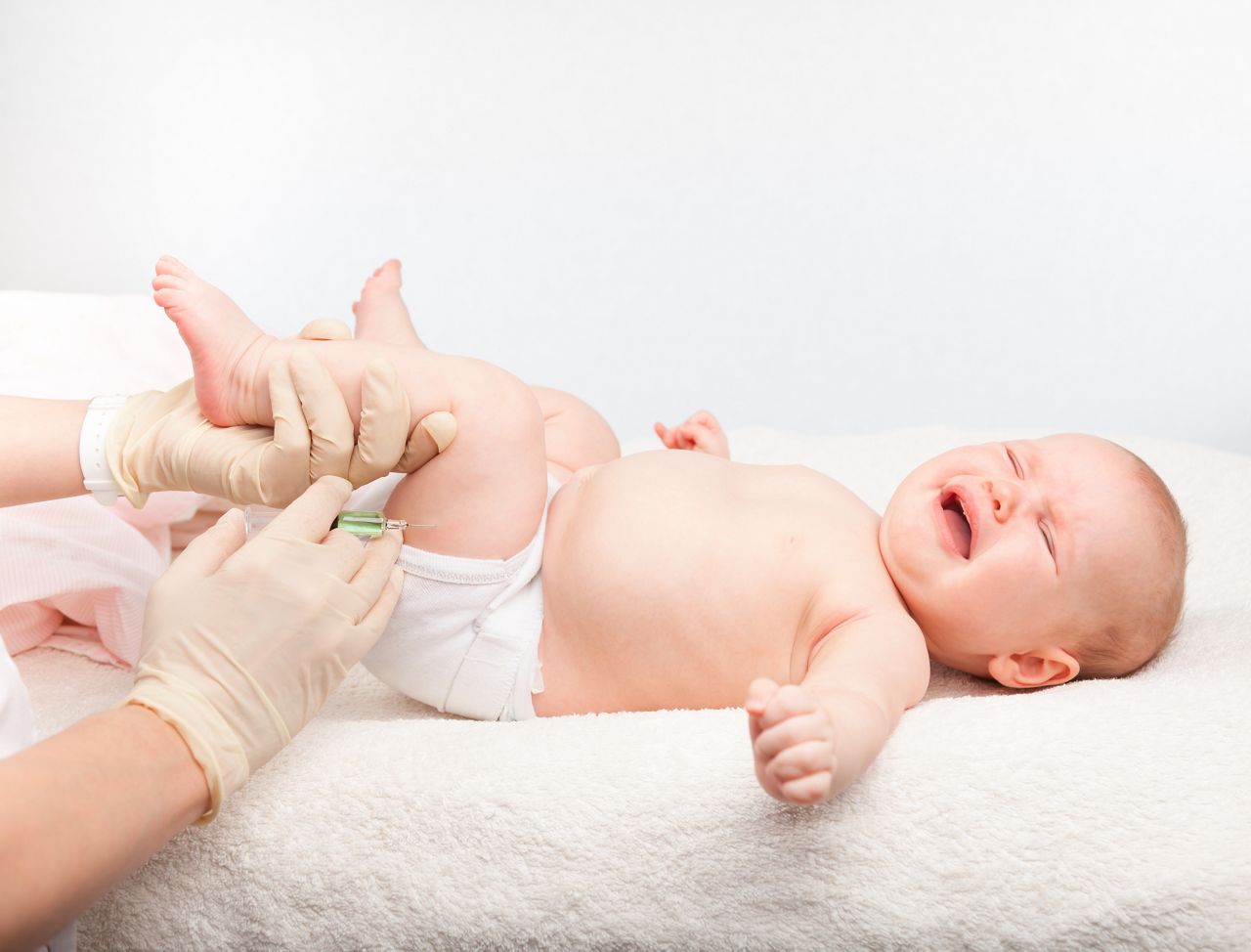 Close-up shot of pediatrician giving a three month baby girl  intramuscular injection in leg