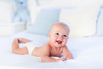 Baby boy wearing diaper in white sunny bedroom. Newborn child relaxing in bed. Nursery for children. Textile and bedding for kids. Family morning at home. New born kid during tummy time with toy bear.; Shutterstock ID 361440518; purchase_order: DNC Thumbnails; job: Articles; client: ; other: 