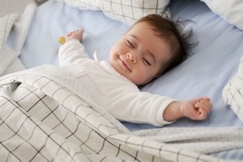 Smiling baby girl lying on a bed sleeping on blue sheets; Shutterstock ID 420756877; purchase_order: DNC Thumbnails; job: Booklets; client: ; other: 