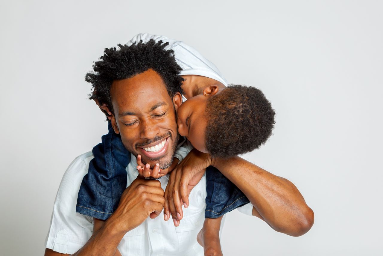 An African American boy on the shoulders of his father, leans over to kiss him on the cheek.  His father laughs with closed eyes.; Shutterstock ID 484650583; purchase_order: DNC Thumbnails; job: Articles; client: ; other: 