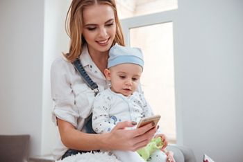 Smiling young mother holding her little son and using cell phone at home; Shutterstock ID 526297141; purchase_order: DNC Thumbnails; job: Webinars 3 (50/188); client: ; other: 
