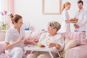 Elderly lady sitting on a couch with a tray and a young nurse giving her medicines in private clinic; Shutterstock ID 530192146; purchase_order: DNC Thumbnails; job: Publications; client: ; other: Replace Fishwife