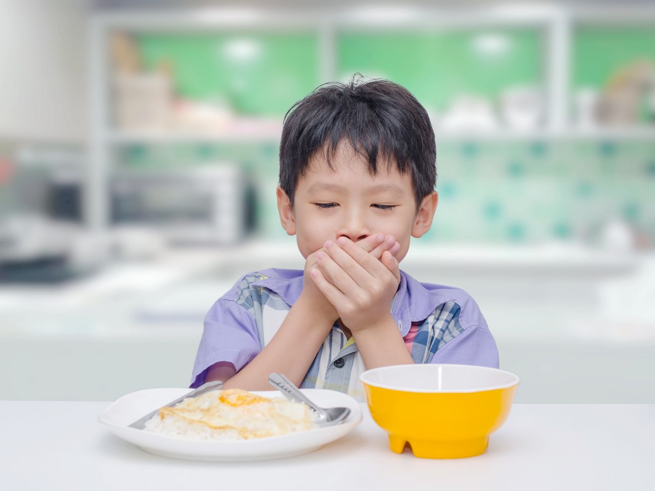 Young asian boy sitting in kitchen and close his mouth by hands between having lunch because he don't want to eat food; Shutterstock ID 592098380; purchase_order: DNC Thumbnails; job: Webinars 2 (50/188); client: ; other: 