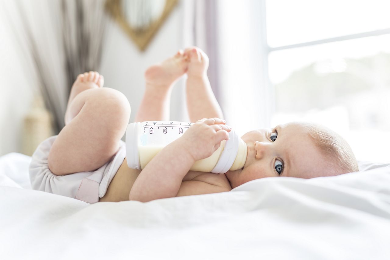 A Pretty baby girl drinks water from bottle lying on bed. Child weared diaper in nursery room.; Shutterstock ID 627983741; purchase_order: DNC Thumbnails; job: Webinars 1 (50/189); client: ; other: 