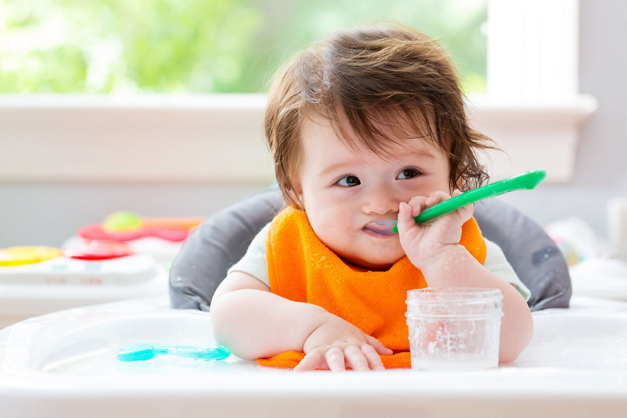 Happy little baby boy eating food with a spoon