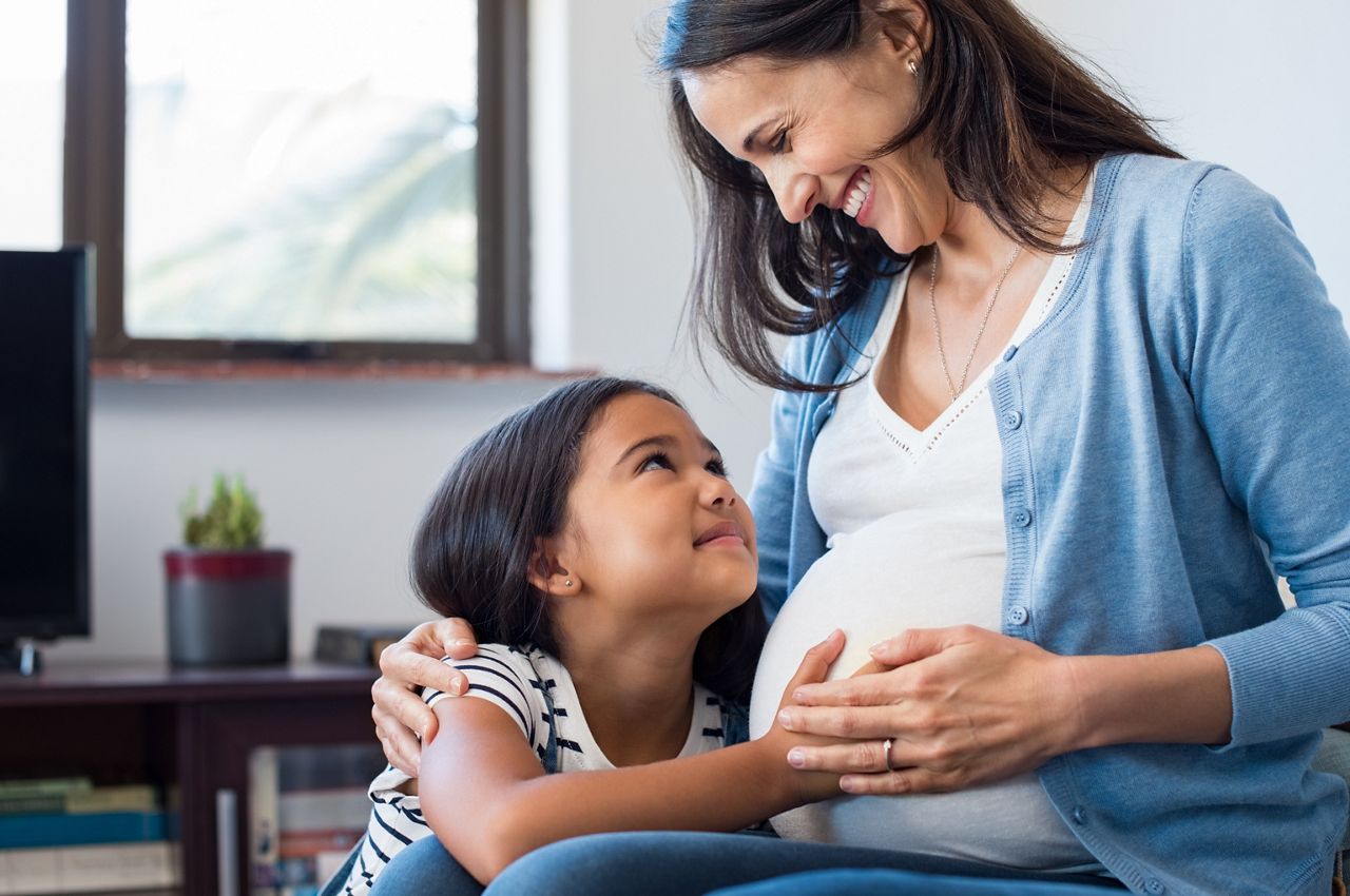 Lovely daughter touching mother's pregnant belly. Happy little girl feeling baby at mother tummy and awaiting the birth of her little brother. Pregnant mother relaxing on sofa with her cute daughter.; Shutterstock ID 705175846; purchase_order: DNC Thumbnails; job: Webinars 4 ; client: ; other: 