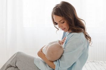 A mother is breastfeeding a baby sitting on a light window background. mother breast feeding and hugging her baby boy; Shutterstock ID 737511223; purchase_order: DNC Thumbnails; job: Webinars 3 (50/188); client: ; other: 