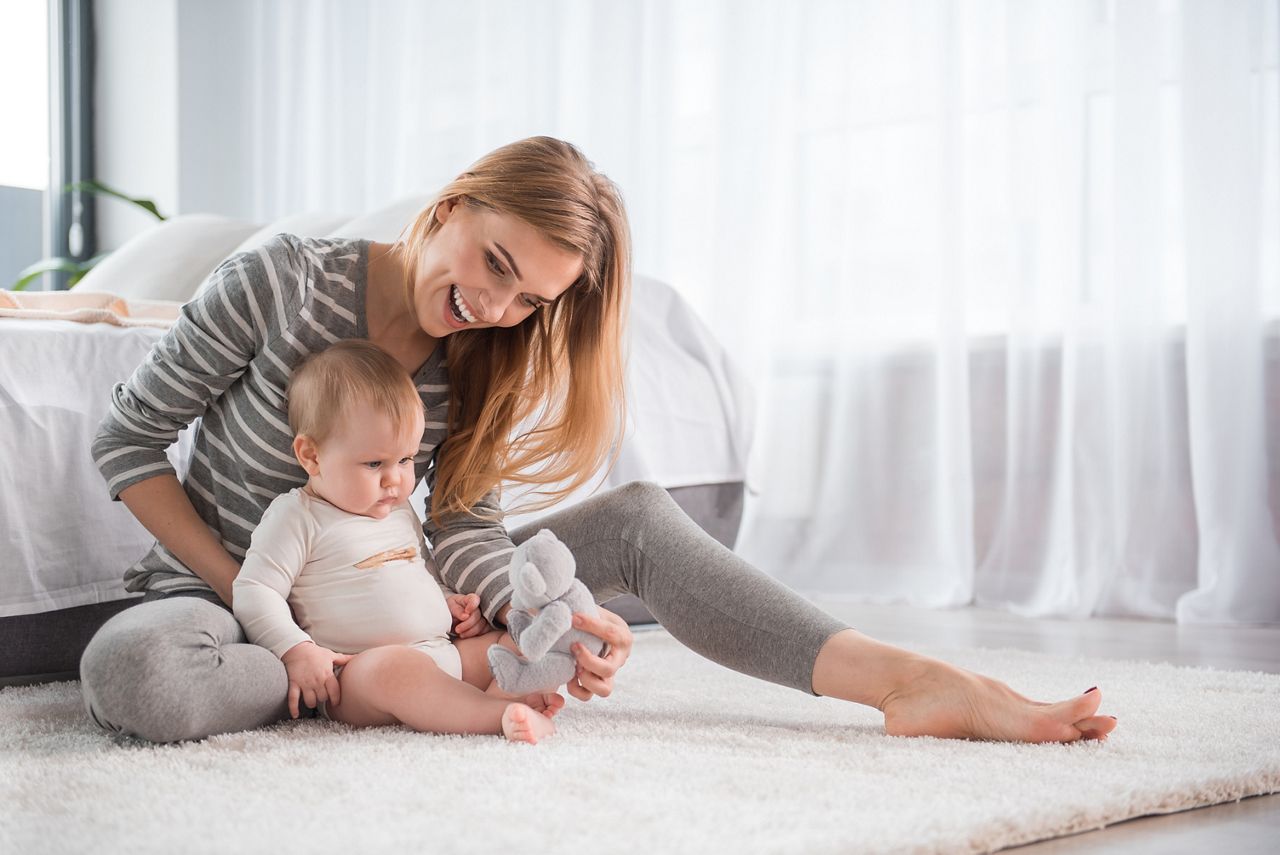 Full length of smiling mother sitting on soft carpet and showing teddy bear to his lovely daughter; Shutterstock ID 784490527; purchase_order: DNC Thumbnails; job: Webinars 1 (50/189); client: ; other: 