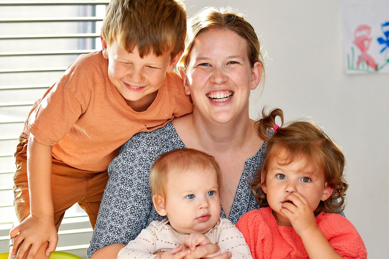 Een moeder zit aan tafel en houdt haar drie kinderen dicht bij zich. 