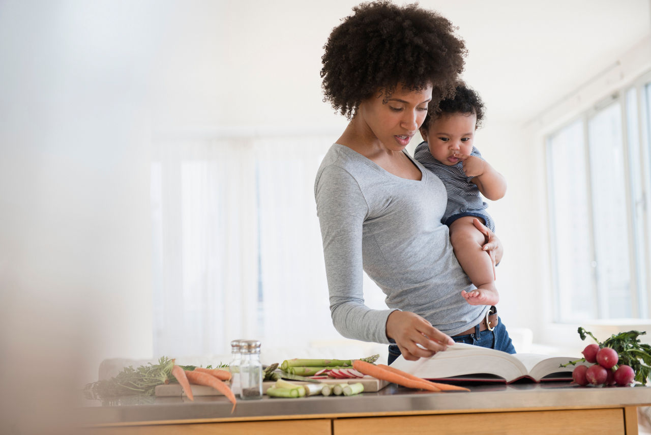 Mother reading cookbook while holding baby son