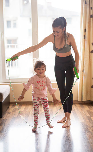 Young mother and daughter stretching with skipping rope at home, mother teaching and having fun with skipping rope.