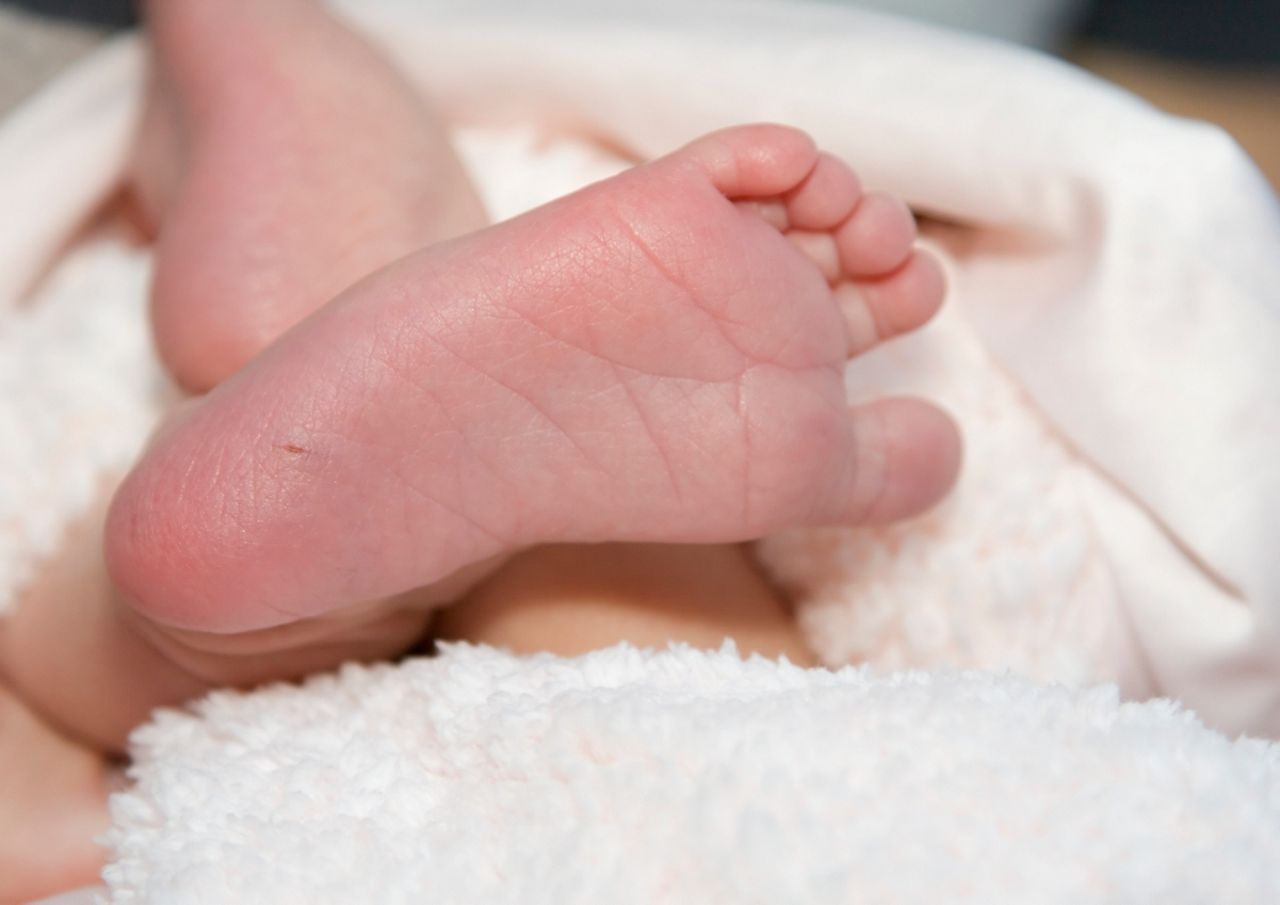 Newborn infant's foot, with mark from blood draw for PKU (phenylketonuria) test. Shallow DOF, focus on heel and blood draw puncture. 