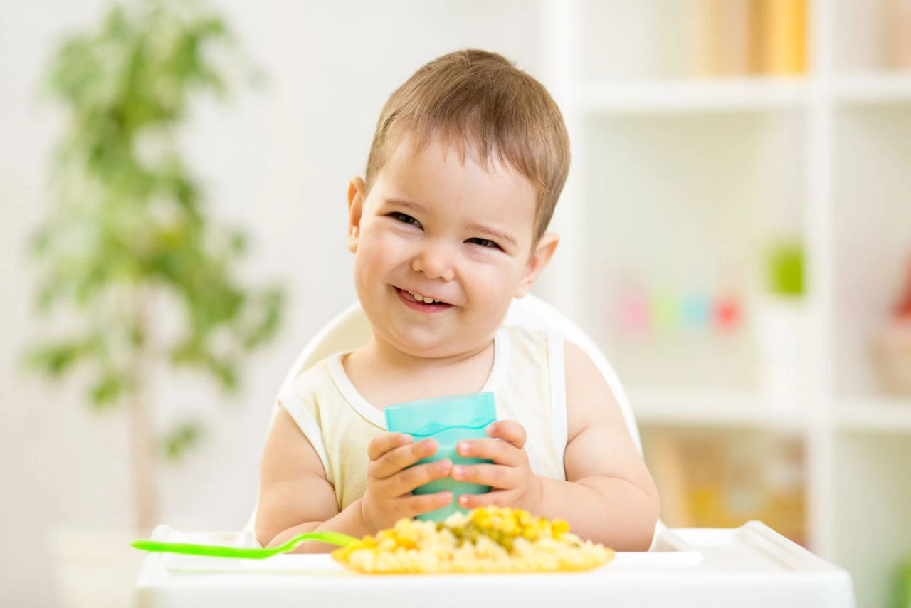 Toddler sitting in a high chair, smiling and holding a drinking cup in his hands