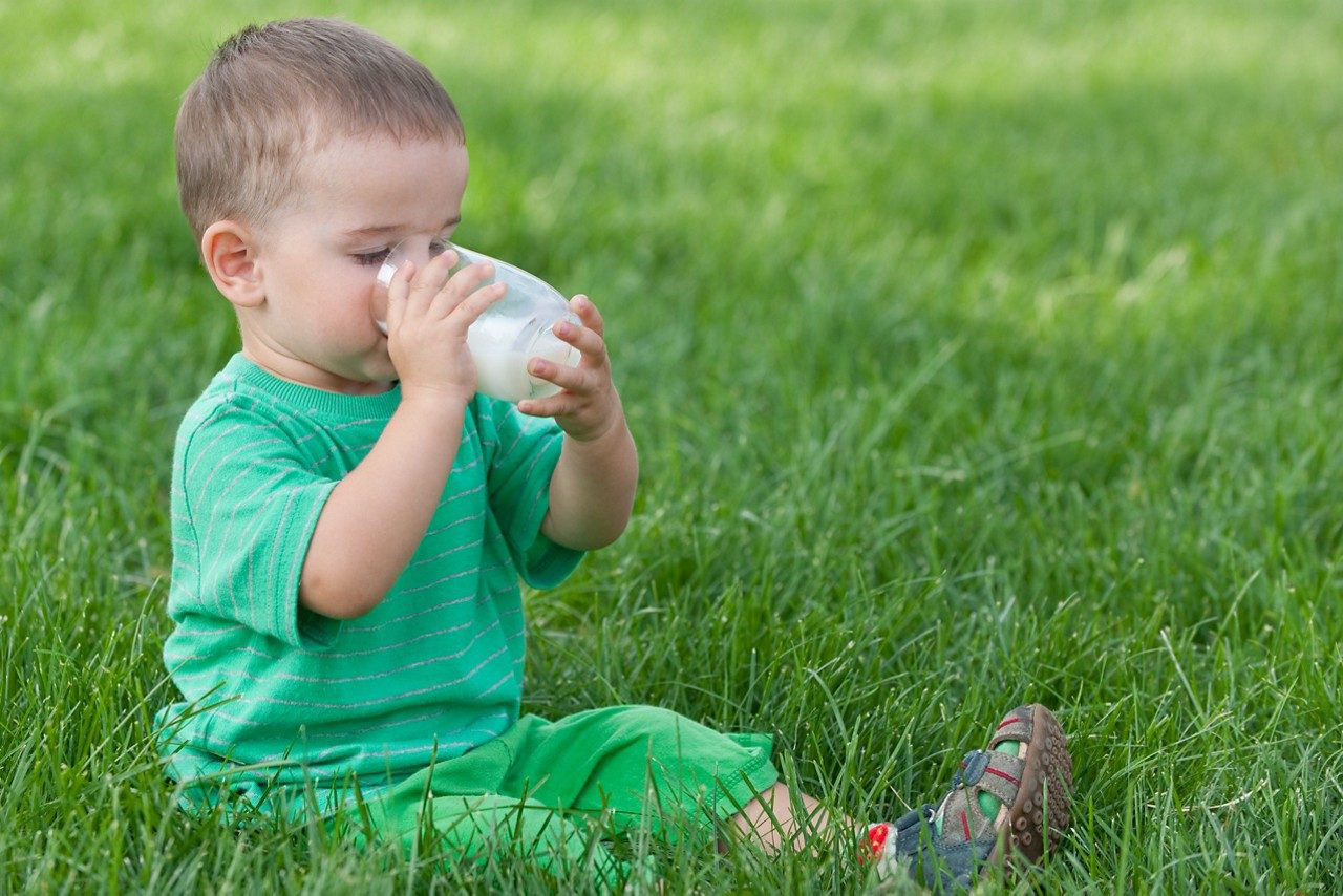 Toddler sitting in the grass enjoying a glass of milk
