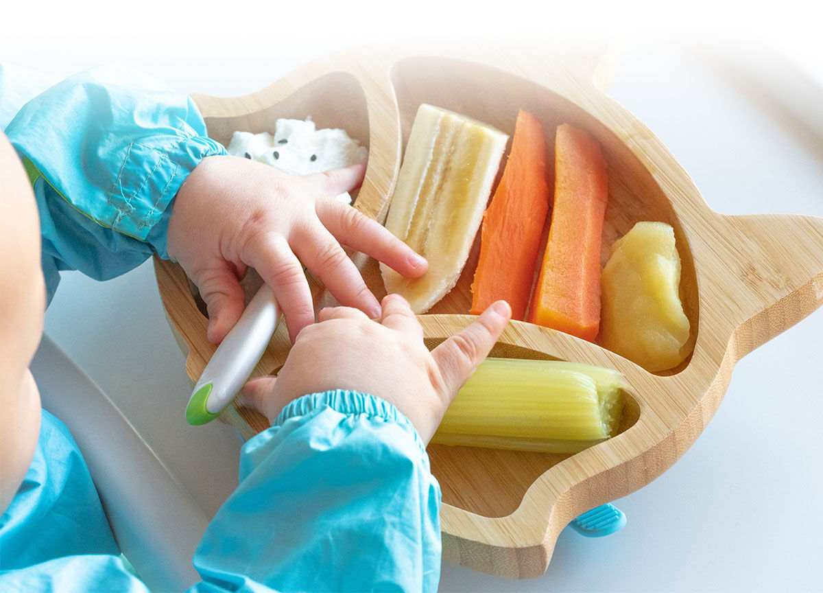 Close-up of a toddler eating vegetables from a plate